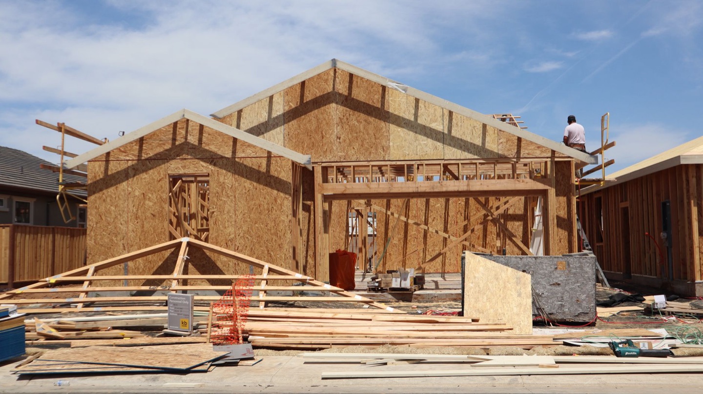 A new single-family home under construction, framed in plywood sheathing, on a sunny day.