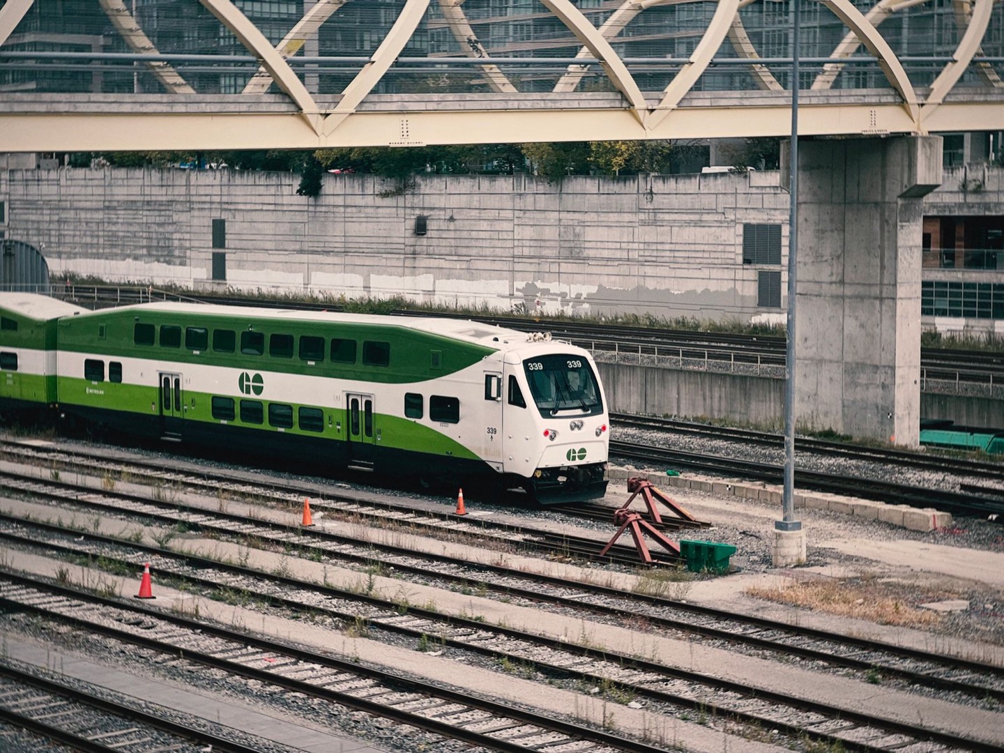 A green and white GO Transit train on the tracks beneath a curved station canopy.