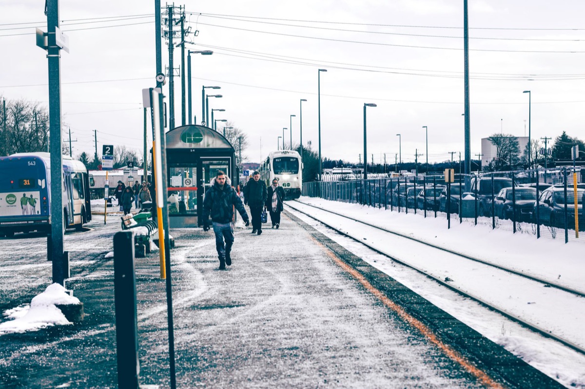 Commuters walk along a snowy GO station platform as a train approaches in winter.