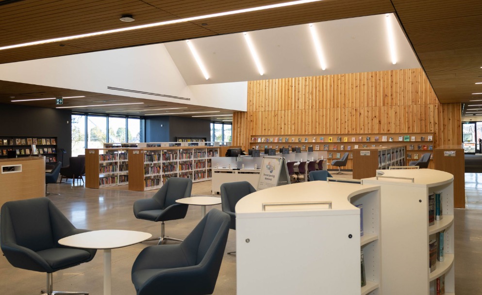 Inside the East Gwillimbury Public Library branch at the HALP Centre, with reading chairs, low shelving, and a timber-clad feature wall.
