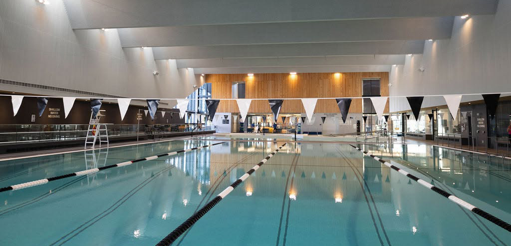 The lap pool at the HALP Centre, with marked swim lanes and championship flags strung overhead.