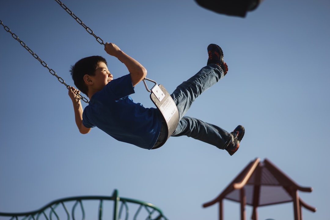 A child mid-swing at a playground against a clear blue sky, with play structures behind.